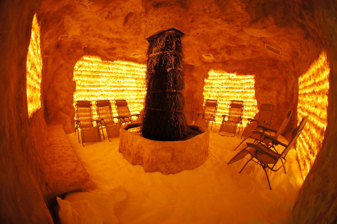 Jasna, pomarańczowa grota solna z leżakami i tężnią solankową pośrodku. Ściany i podłoga pokryte solą, tworzące ciepły, relaksujący klimat.