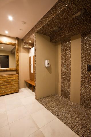 Nowoczesna kabina prysznicowa z mozaiką w odcieniach brązu i beżu, drewniane elementy wykończenia, lustro w ozdobnej ramie. Całość utrzymana w ciepłej tonacji.