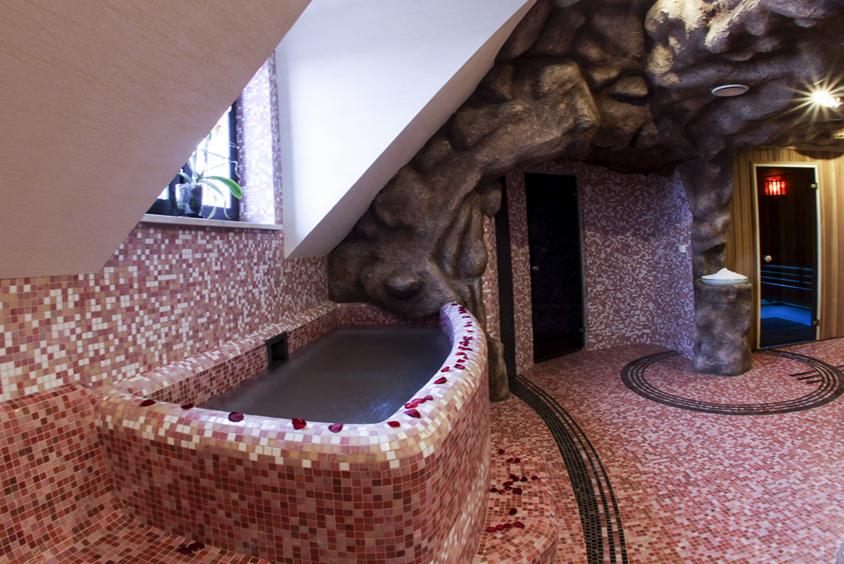 Luksusowa sauna z mozaikową wanną i ścianami imitującymi skałę, oświetlona punktowo, z dekoracyjnymi płatkami róż. Unikalny design wnętrza sauny.