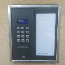 Zamontowany panel domofonowy ACO z klawiaturą numeryczną i listą lokatorów na elewacji budynku. Widoczne przyciski i wyświetlacz.