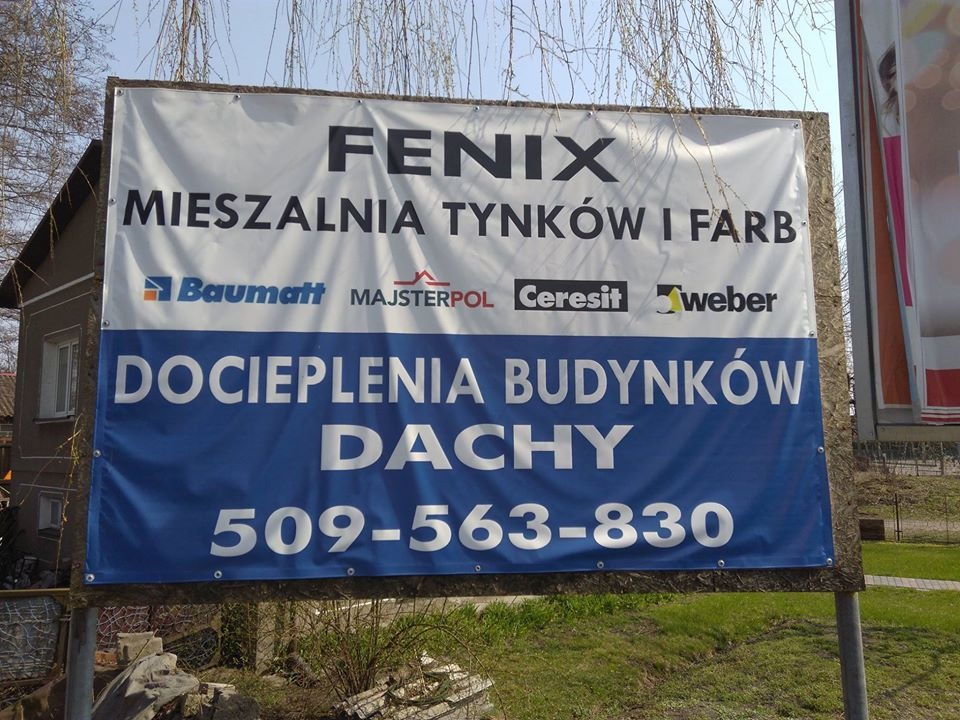 Billboard reklamowy firmy Fenix, oferującej mieszalnię tynków i farb, docieplenia budynków i dachy, z numerem telefonu, umieszczony przy drodze na tle drzew i budynku.