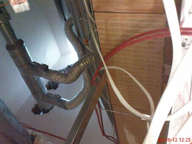 Fragment instalacji przeciwpożarowej z rurami aluminiowymi i przewodami elektrycznymi, widoczne elementy mocujące i drewniana konstrukcja w tle.