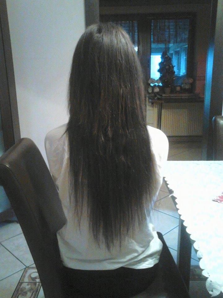 Długie, ciemne włosy kobiety siedzącej tyłem na krześle. W tle okno z dekoracją świąteczną i fragment pomieszczenia z białą ścianą.