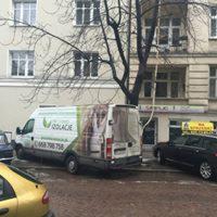 Samochód dostawczy z logo firmy ociepleniowej zaparkowany przed budynkiem mieszkalnym w pochmurny dzień.