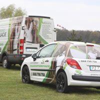 Dwa samochody firmowe z grafiką reklamującą usługi ocieplania, zaparkowane na trawie. Na samochodach widoczne numery telefonów i logo firmy.