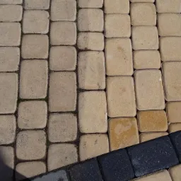 Fragment chodnika z kostki brukowej, część wyczyszczona, część zabrudzona, widoczne ciemne obrzeże.