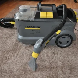 Profesjonalny odkurzacz piorący Kärcher Puzzi 10/1 na brązowym dywanie z długim włosiem, widoczne detale konstrukcyjne i elementy sterujące w kolorze żółtym.