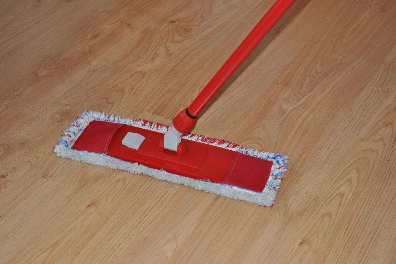 Czerwony mop płaski z mikrofibry na drewnianej podłodze podczas procesu czyszczenia.