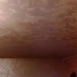 Ściany i sufit w pomieszczeniu pokryte dekoracyjną, brązowo-złotą strukturą imitującą chmurki, z widocznym oświetleniem górnym.