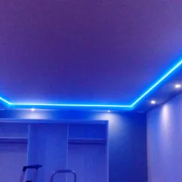 Pokój z sufitem podwieszanym z niebieskim oświetleniem LED, widoczne również halogeny i ściana z dekoracyjną cegłą.