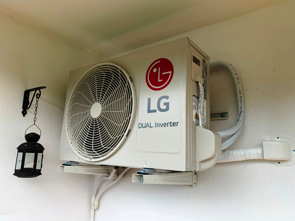 Zewnętrzna jednostka klimatyzacji LG Dual Inverter zamontowana na ścianie, z dekoracyjną czarną latarnią wiszącą obok.