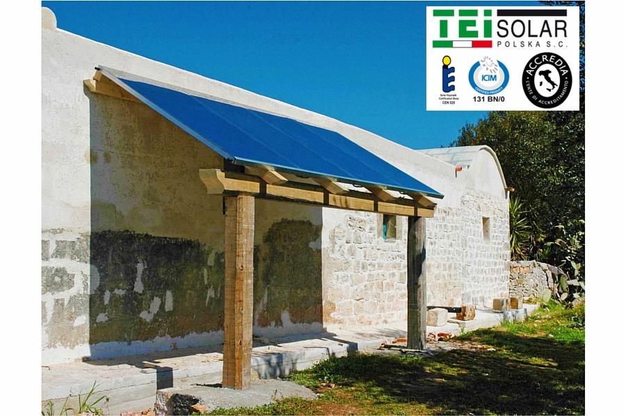 Niebieski panel słoneczny zamontowany na drewnianej konstrukcji przy budynku z kamienia, logo TEI SOLAR w prawym górnym rogu.