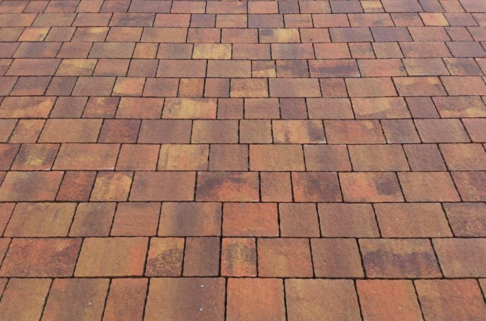 Ułożona, ceglasto-pomarańczowa kostka betonowa tworząca wzór chodnika. Widoczna struktura i kolorystyka poszczególnych elementów. Ujęcie z perspektywy.