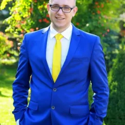 Uśmiechnięty mężczyzna w niebieskim garniturze i żółtym krawacie na tle zieleni. W prawym górnym rogu logo Aviva.