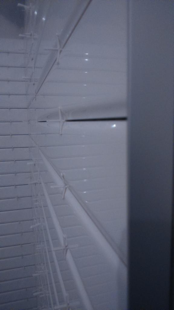 Białe, poziome żaluzje okienne, widoczne pod kątem, z metalową ramą po prawej stronie. Delikatne refleksy światła na powierzchni lameli.