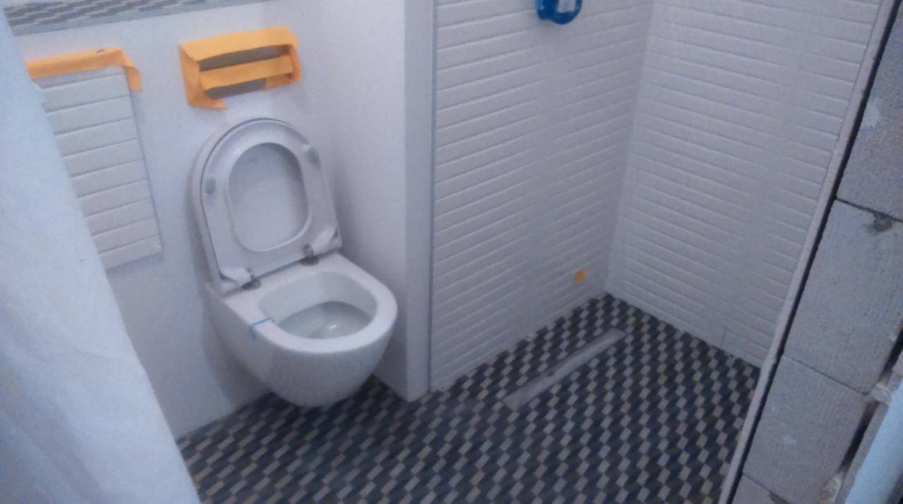 Nowoczesna toaleta w łazience po remoncie. Biała ceramika, wzorzysta podłoga i świeżo pomalowane ściany. Detale zabezpieczone folią malarską.