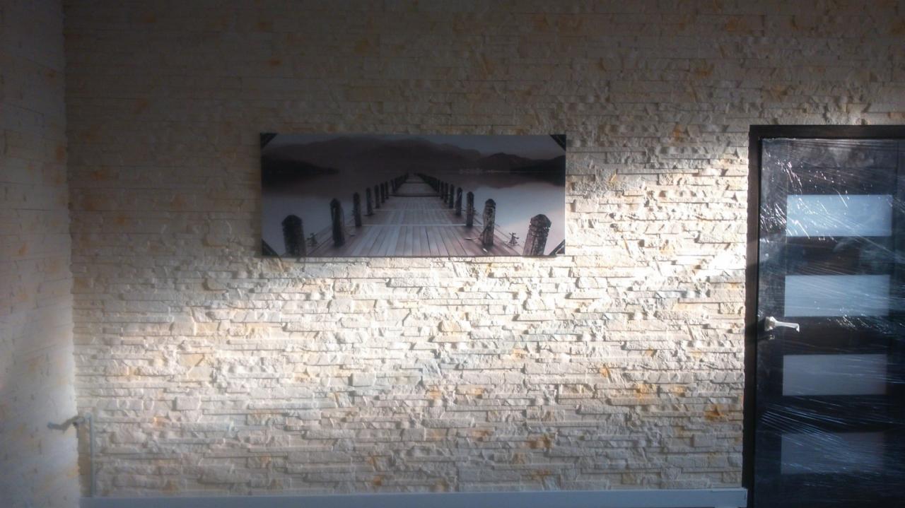 Ściana z dekoracyjnej, jasnej cegły z obrazem mola i zamkniętymi drzwiami. Ujęcie z niskiego kąta, podkreślające fakturę ściany i detale wykończenia.