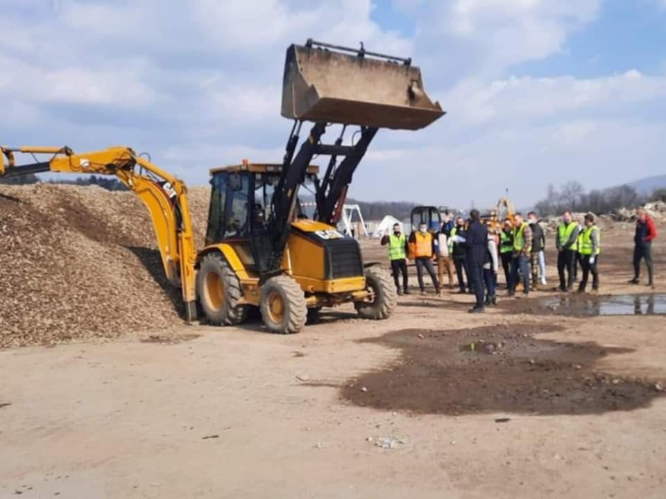 Żółta koparko-ładowarka CAT na placu budowy z grupą osób w odblaskowych kamizelkach, prawdopodobnie podczas szkolenia z obsługi maszyn.