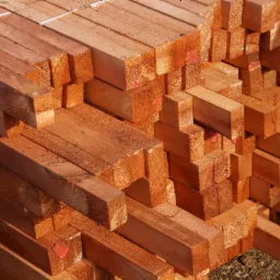 Stos tarcicy budowlanej z widocznym logo tartaku, ukazujący regularne ułożenie i naturalną barwę drewna, z detalami faktury i oznaczeniami na niektórych elementach.