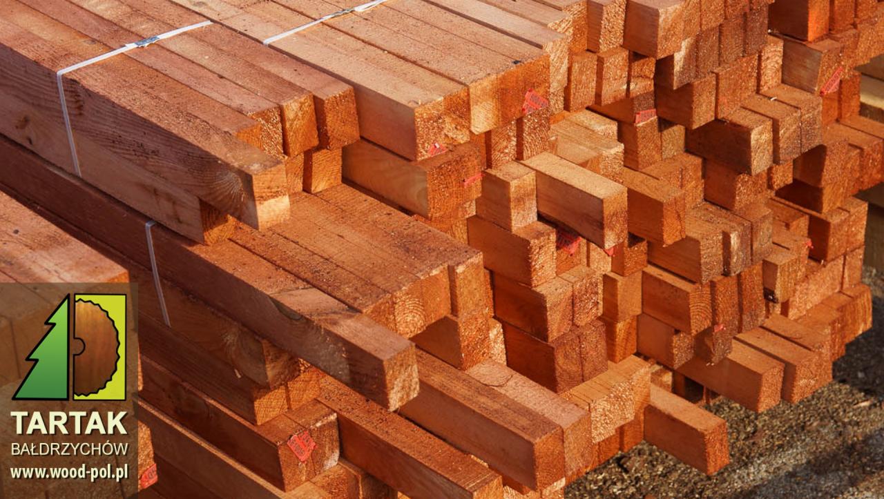 Stos tarcicy budowlanej z widocznym logo tartaku, ukazujący regularne ułożenie i naturalną barwę drewna, z detalami faktury i oznaczeniami na niektórych elementach.