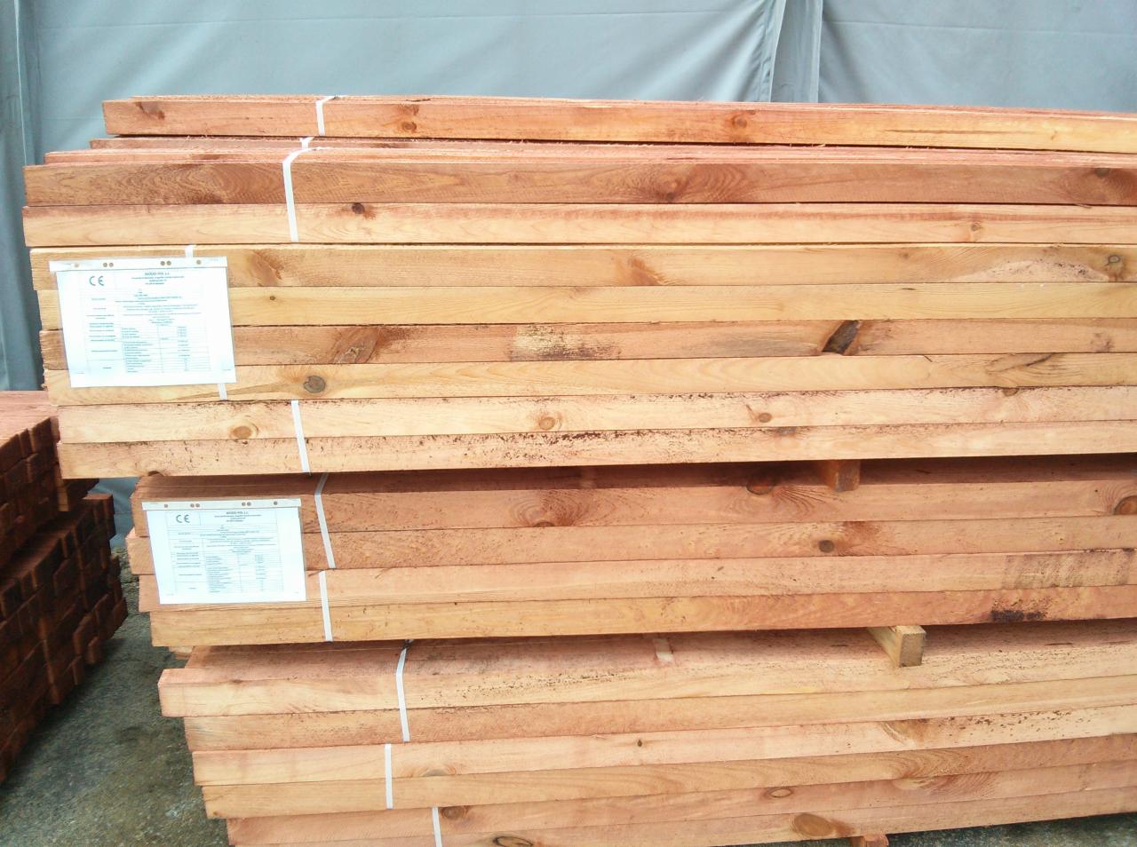 Stosy tarcicy budowlanej z certyfikatami CE, zabezpieczone taśmą, w magazynie w Poddębicach. Widoczne słoje drewna i naturalna kolorystyka.