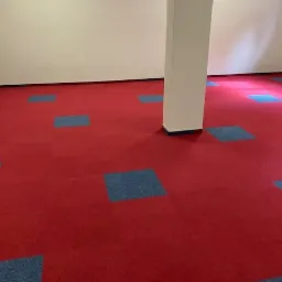 Czerwona podłoga z kwadratowymi, niebieskimi wstawkami, widoczny biały filar w pomieszczeniu.