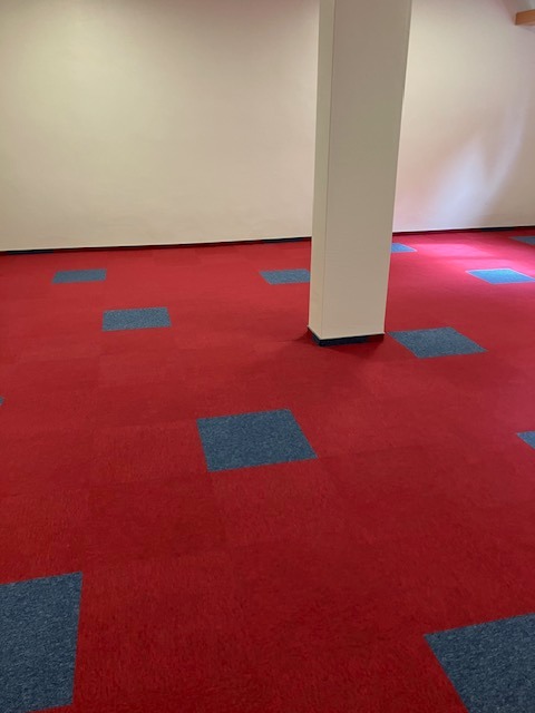 Czerwona podłoga z kwadratowymi, niebieskimi wstawkami, widoczny biały filar w pomieszczeniu.