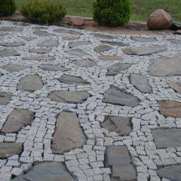 Zakład Budowlany - Ułożona kostka granitowa z nieregularnymi płytami kamiennymi w ogrodzie, z widocznymi krzewami i kamieniami w tle.