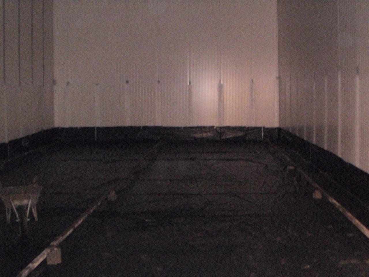 Przygotowanie podłoża: czarna folia izolacyjna rozłożona na podłodze, listwy poziomujące. Ściany w tle z pionowymi panelami. W rogu widoczny element rusztowania.