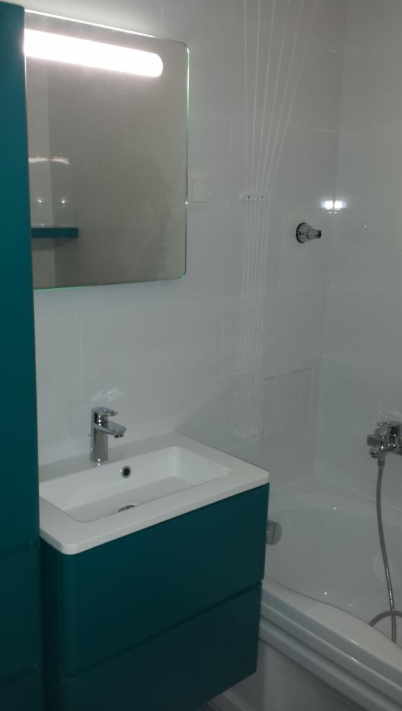 Nowoczesna łazienka: białe płytki, turkusowa szafka z umywalką, lustro z oświetleniem i wanna. Minimalistyczny design, chromowana armatura.