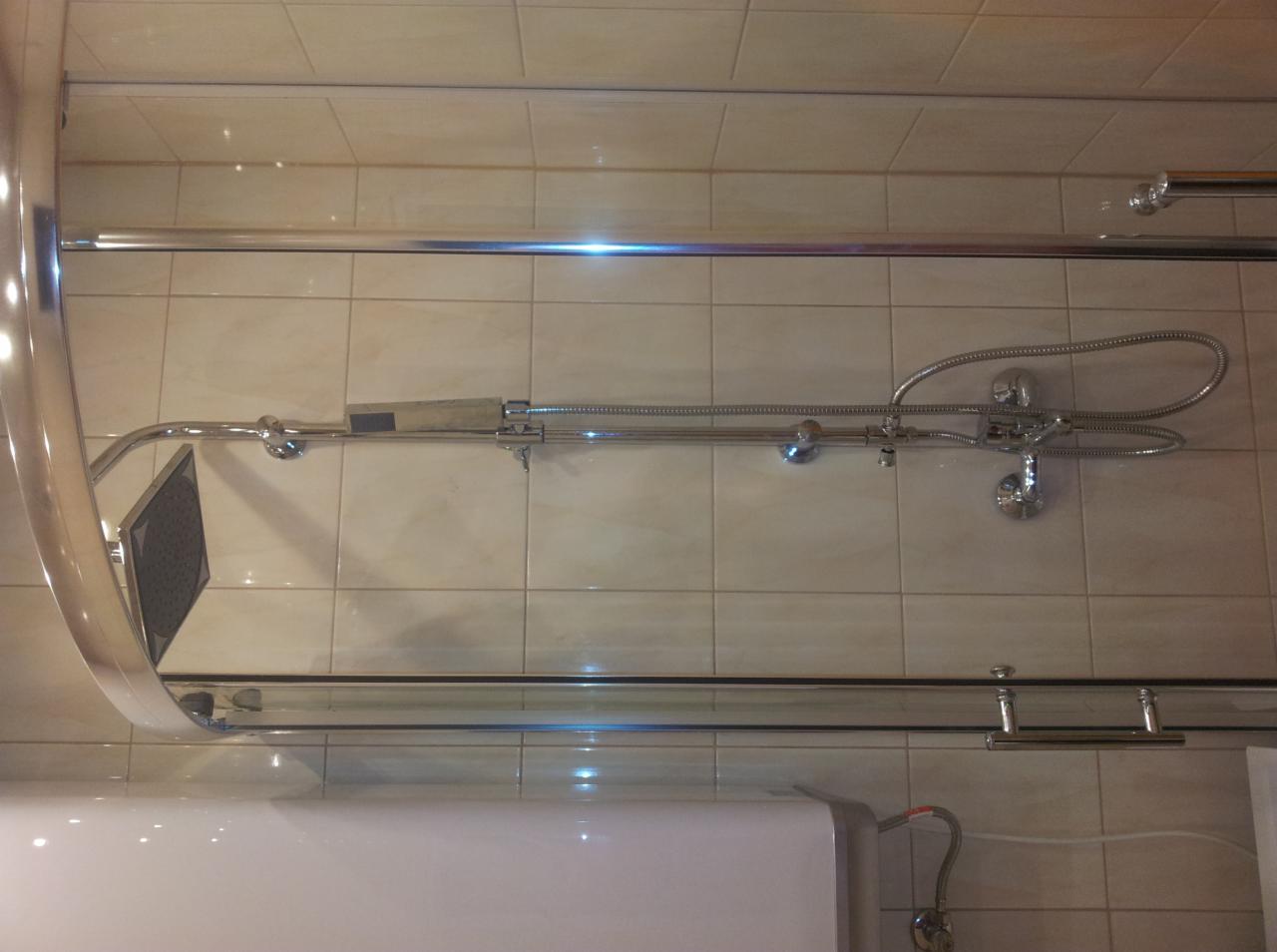 Zamontowany zestaw prysznicowy z deszczownicą na tle beżowych płytek, widoczny bojler. Chromowana armatura łazienkowa po instalacji.