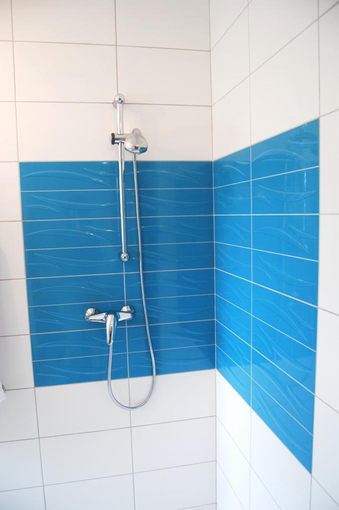 Wykończona kabina prysznicowa z niebieskimi, falowanymi płytkami na ścianie i chromowaną armaturą, prezentująca nowoczesny design łazienki.