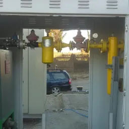 Otwarta szafka z żółtymi elementami instalacji gazowej, widok na ulicę i samochód osobowy w tle.