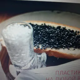 Szklanka z białym granulatem i czarne granulki na kromce chleba, prezentacja surowców do produkcji tkanin z tworzyw sztucznych.