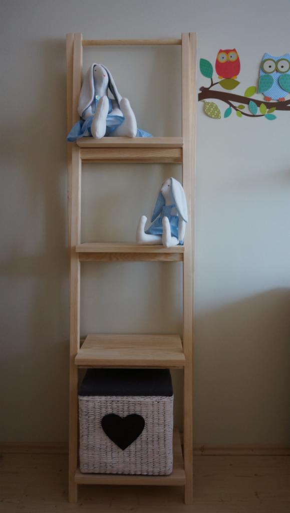 Drewniana drabina-regał z trzema półkami, na których znajdują się pluszowe króliki w niebieskich sukienkach i wiklinowy kosz z czarnym sercem, na ścianie naklejka z sowami.