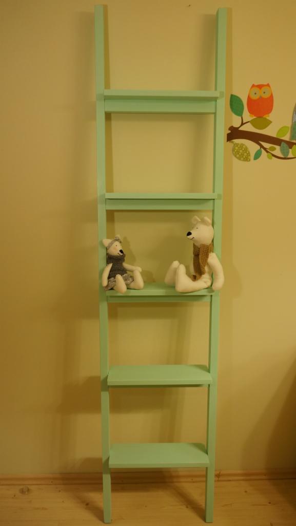 Jasnozielona, drewniana drabina-regał z trzema półkami, na których siedzą dwa pluszowe misie, ustawiona na tle żółtej ściany z naklejką sowy.