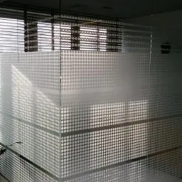 Szklana ścianka działowa w biurze z dekoracyjnym wzorem w kropki, przez którą widać żaluzje okienne. Nowoczesny design, doświetlenie naturalnym światłem.