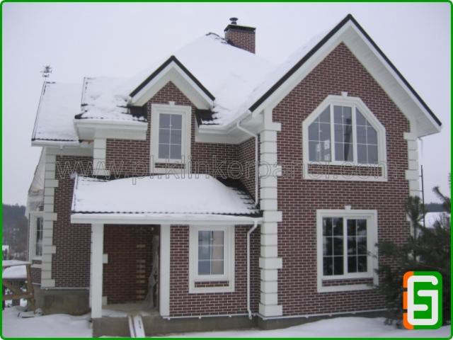 Dom z cegły klinkierowej, ośnieżony dach i białe detale architektoniczne. Prezentacja elewacji budynku w Pucku w zimowej scenerii.