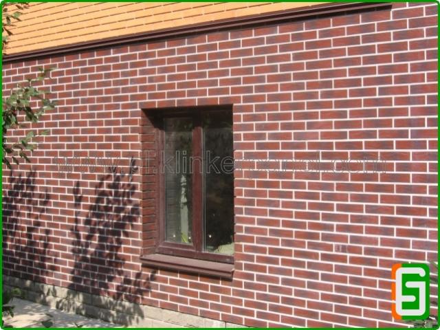 Elewacja budynku wykończona czerwoną cegłą klinkierową z białymi fugami, widoczne okno i cień drzewa. Estetyczne wykończenie zewnętrzne budynku.