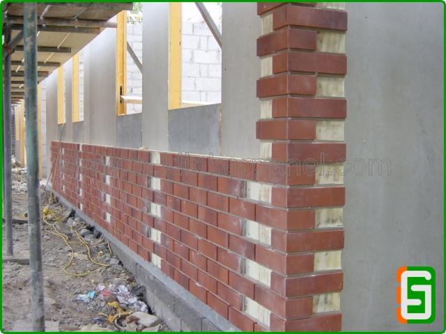 Murowanie elewacji z cegły klinkierowej z widoczną izolacją. Częściowo wykończona ściana budynku w trakcie budowy, z rusztowaniem w tle.