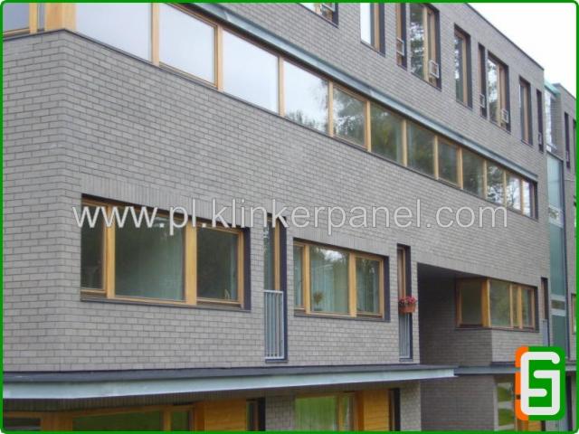 Elewacja budynku wykończona szarą cegłą klinkierową z drewnianymi oknami. Widoczne detale architektoniczne i poziome linie okien.