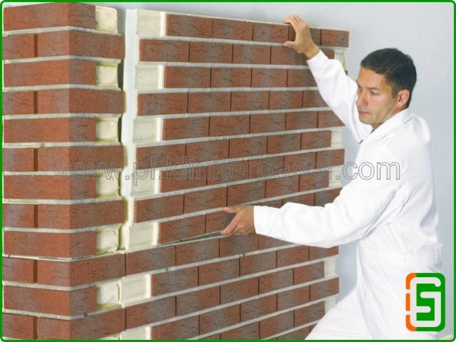 Mężczyzna w białym kombinezonie montuje panele elewacyjne imitujące cegłę na ocieplonej ścianie. Widoczna struktura i warstwy izolacyjne.