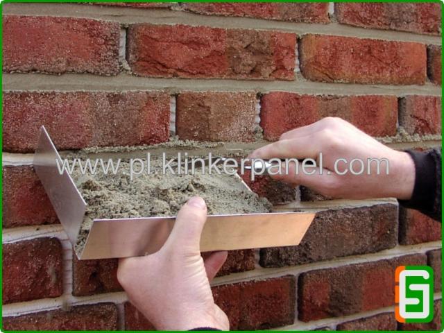 Aplikacja zaprawy na ceglany mur klinkierowy za pomocą metalowej kielni. Widoczne spoiny między cegłami. Detal pracy murarskiej.