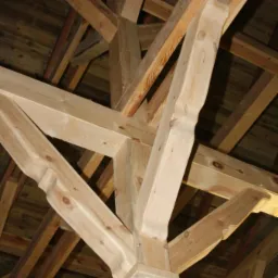 Drewniana konstrukcja dachu z elementami dekoracyjnymi, widok od dołu, eksponujący połączenia belek i słupów.