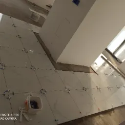 Układanie białych płytek podłogowych z marmurowym wzorem, z użyciem krzyżyków dystansowych, w trakcie prac wykończeniowych w pomieszczeniu.