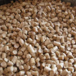 Jasnobrązowe granulki biomasy drzewnej, widoczne w metalowym pojemniku, z delikatnymi ciemniejszymi plamkami na powierzchni.