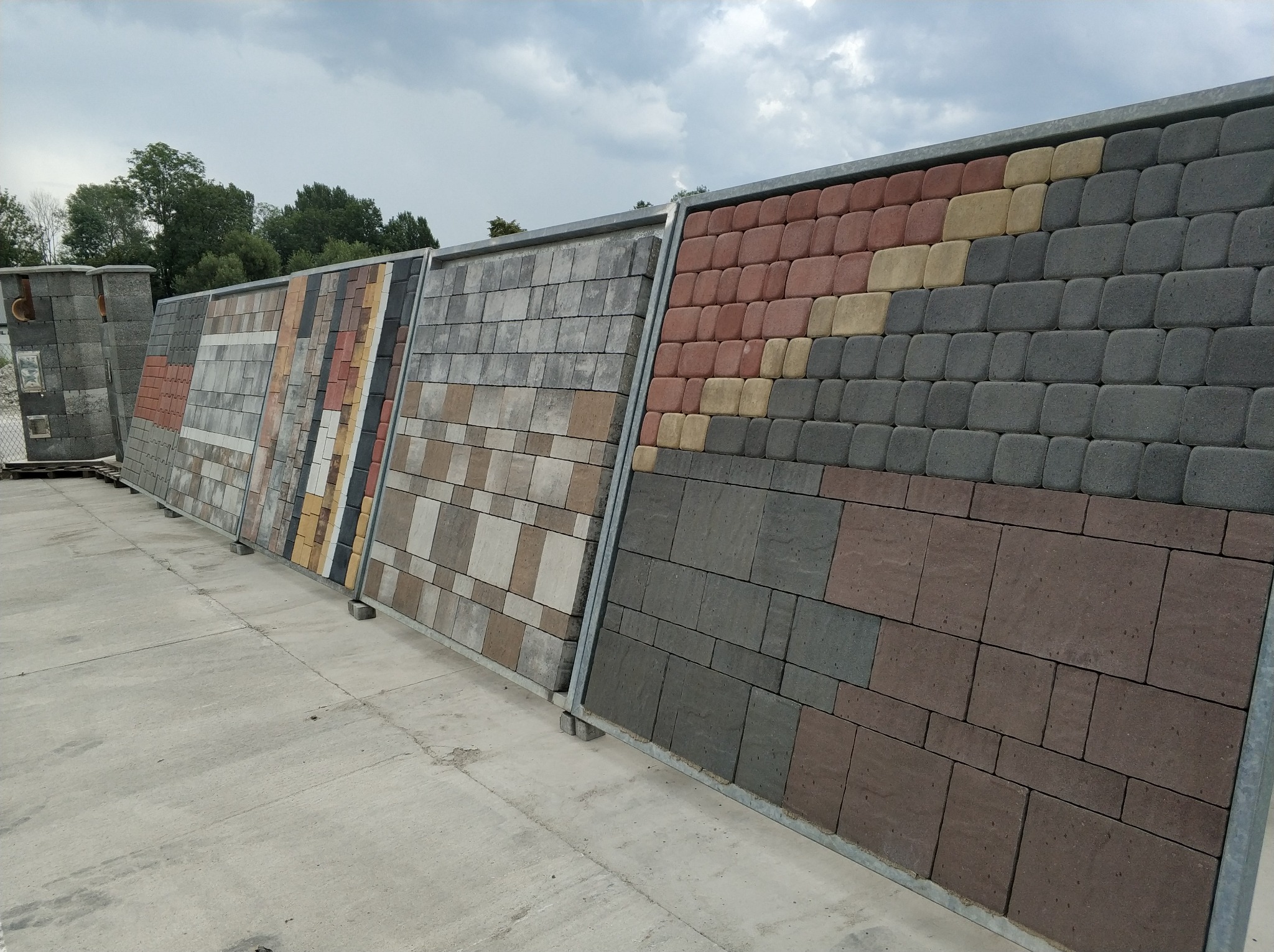 Ekspozycja różnorodnych wzorów i kolorów kostki brukowej na stojakach, prezentująca tekstury i układy.