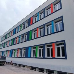 SKLADOKIEN.PL Sp. z o.o. - Budynek szkoły po renowacji elewacji z nowymi oknami i kolorowymi elementami dekoracyjnymi. Widoczny fragment terenu budowy i samochód dostawczy.