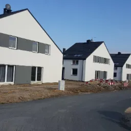 Surowe domki szeregowe w Opolu, z białymi elewacjami i ciemnymi dachami, jeszcze w trakcie wykończenia terenu, zabezpieczone znakami drogowymi.