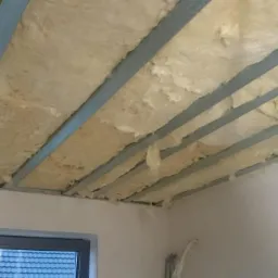 Poddasze w Nowym Wiśniczu w trakcie ocieplania wełną mineralną, widoczne metalowe profile konstrukcyjne sufitu podwieszanego i fragment okna.